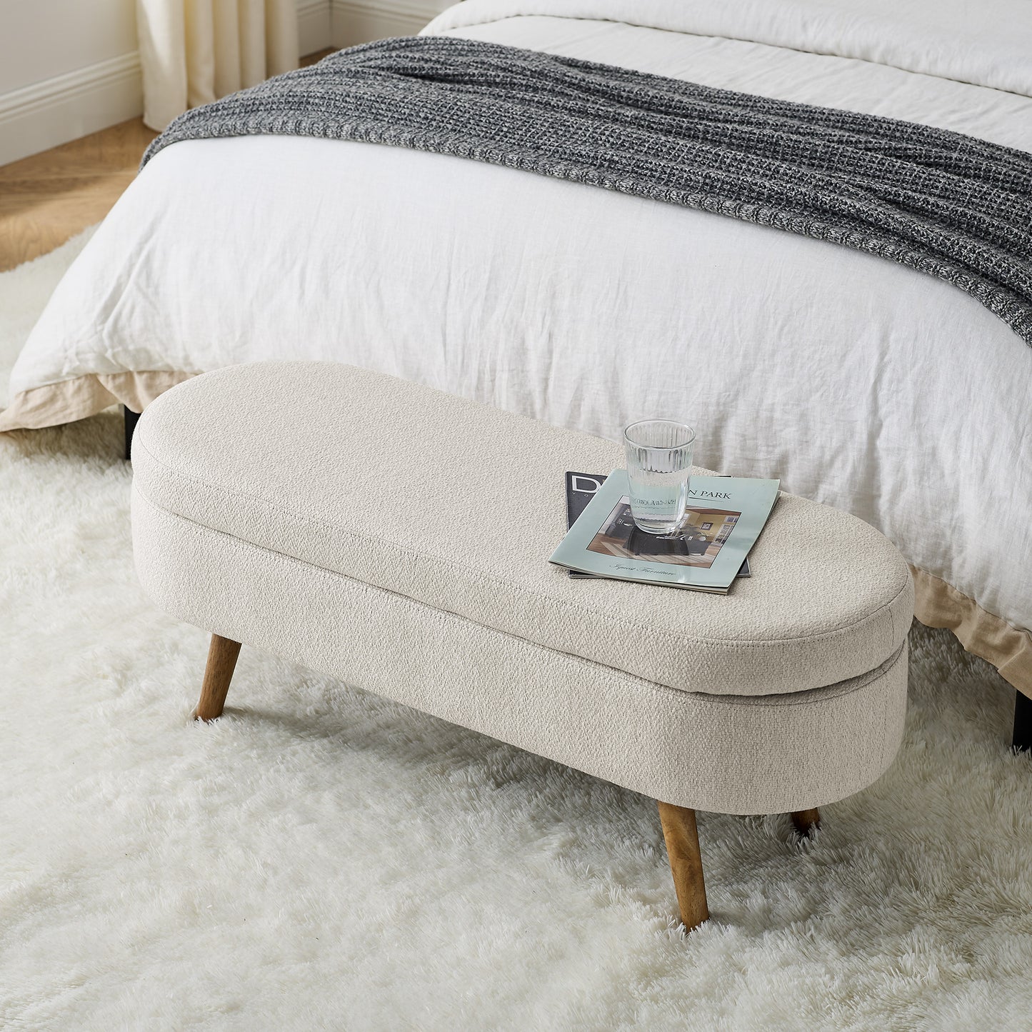 Oval upholstered storage bench in cream boucle fabric with wooden legs