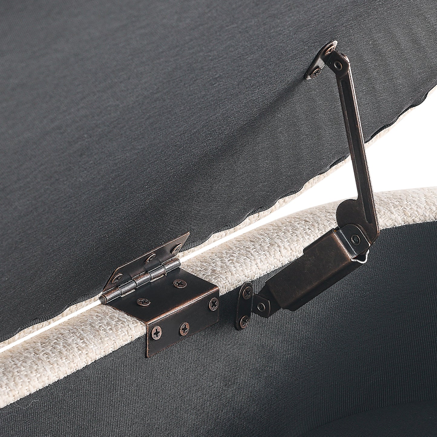 Antique bronze hinge detail on a grey upholstered storage ottoman