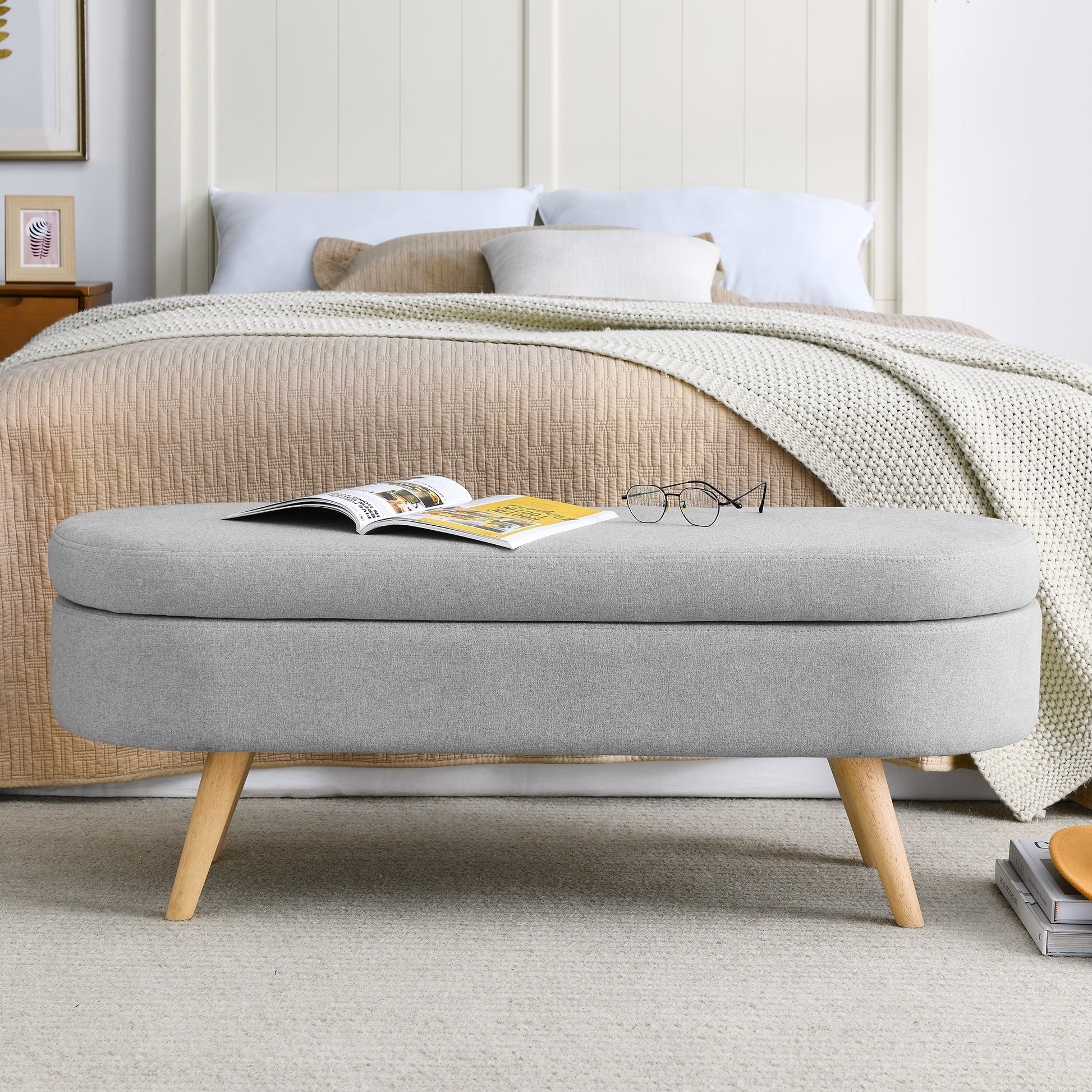 Grey fabric storage ottoman with wooden legs at foot of bed