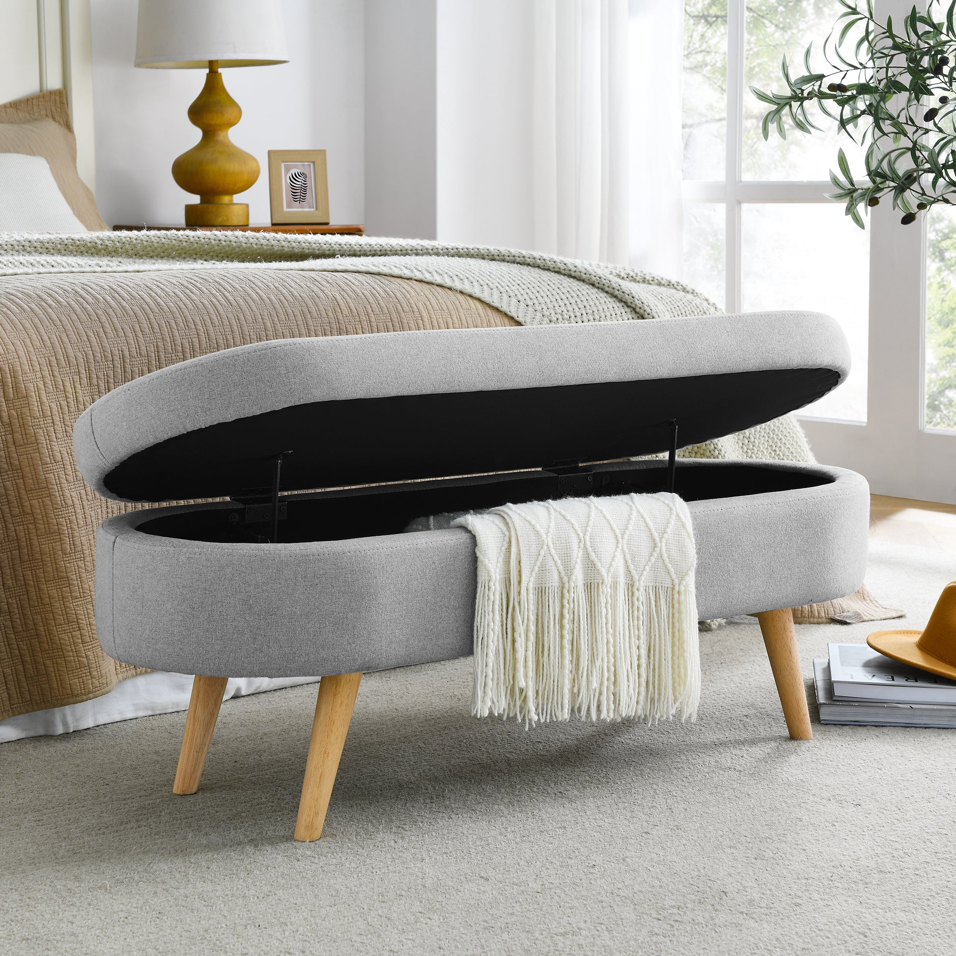 Grey fabric storage ottoman with open lid and white throw