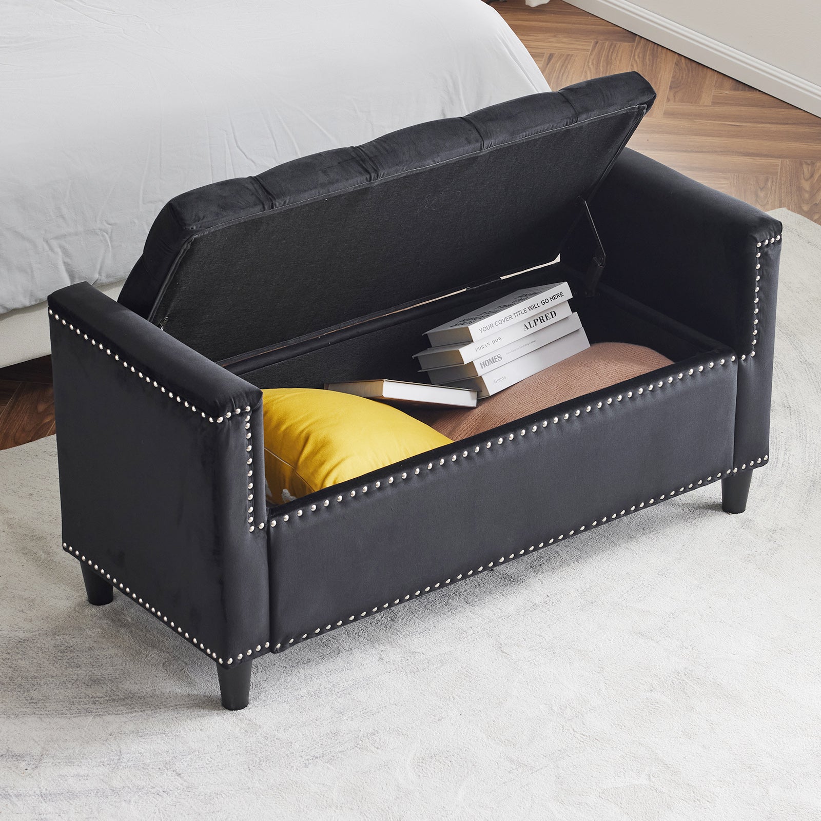 Black velvet storage ottoman with silver nailhead trim and tufted lid open revealing books