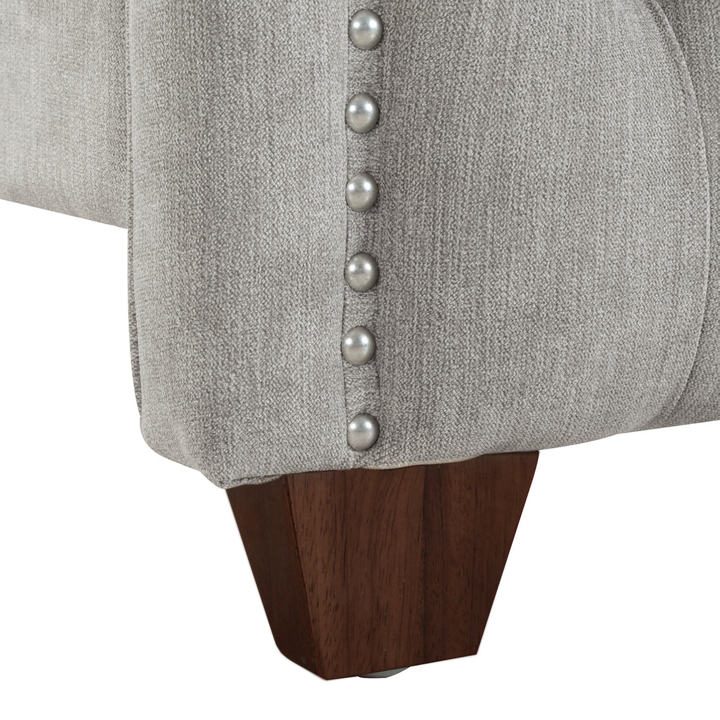 Closeup of upholstered sofa base with silver nailhead trim and dark wood leg