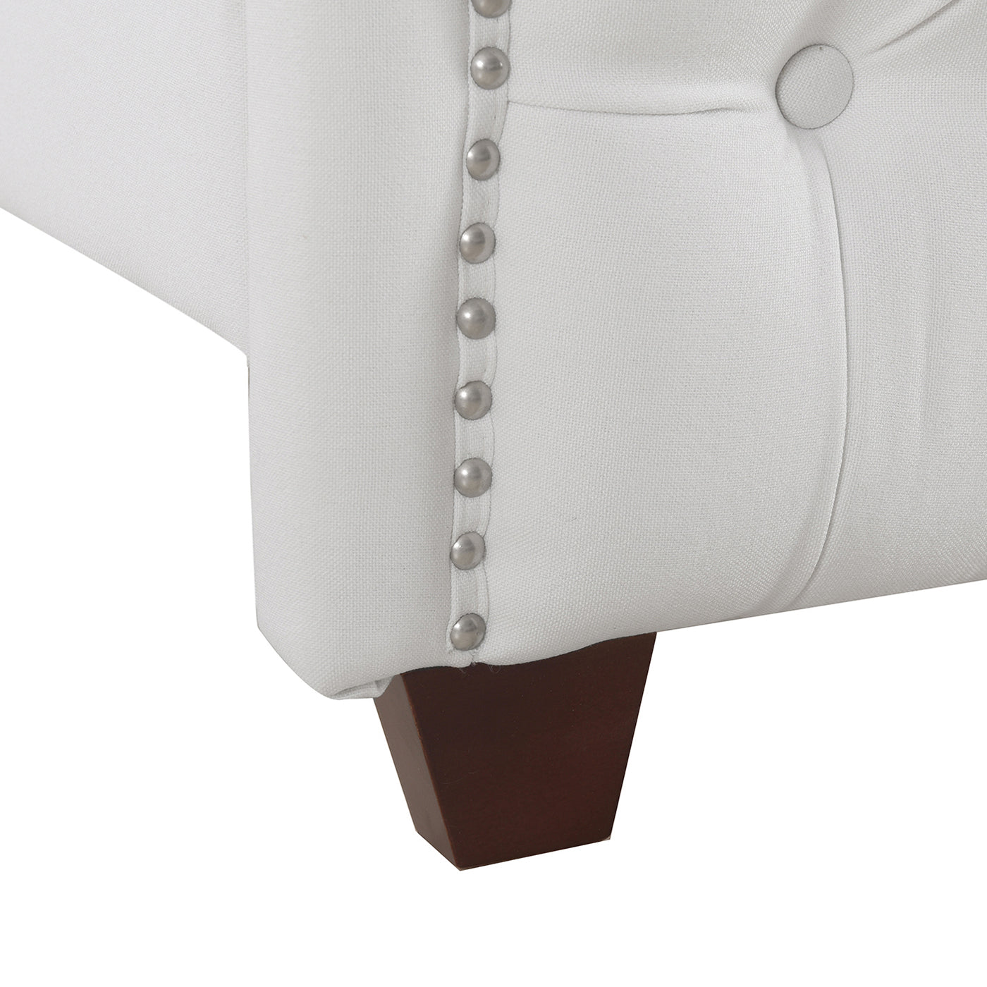 White linen tufted sofa corner with nailhead trim and dark wood leg