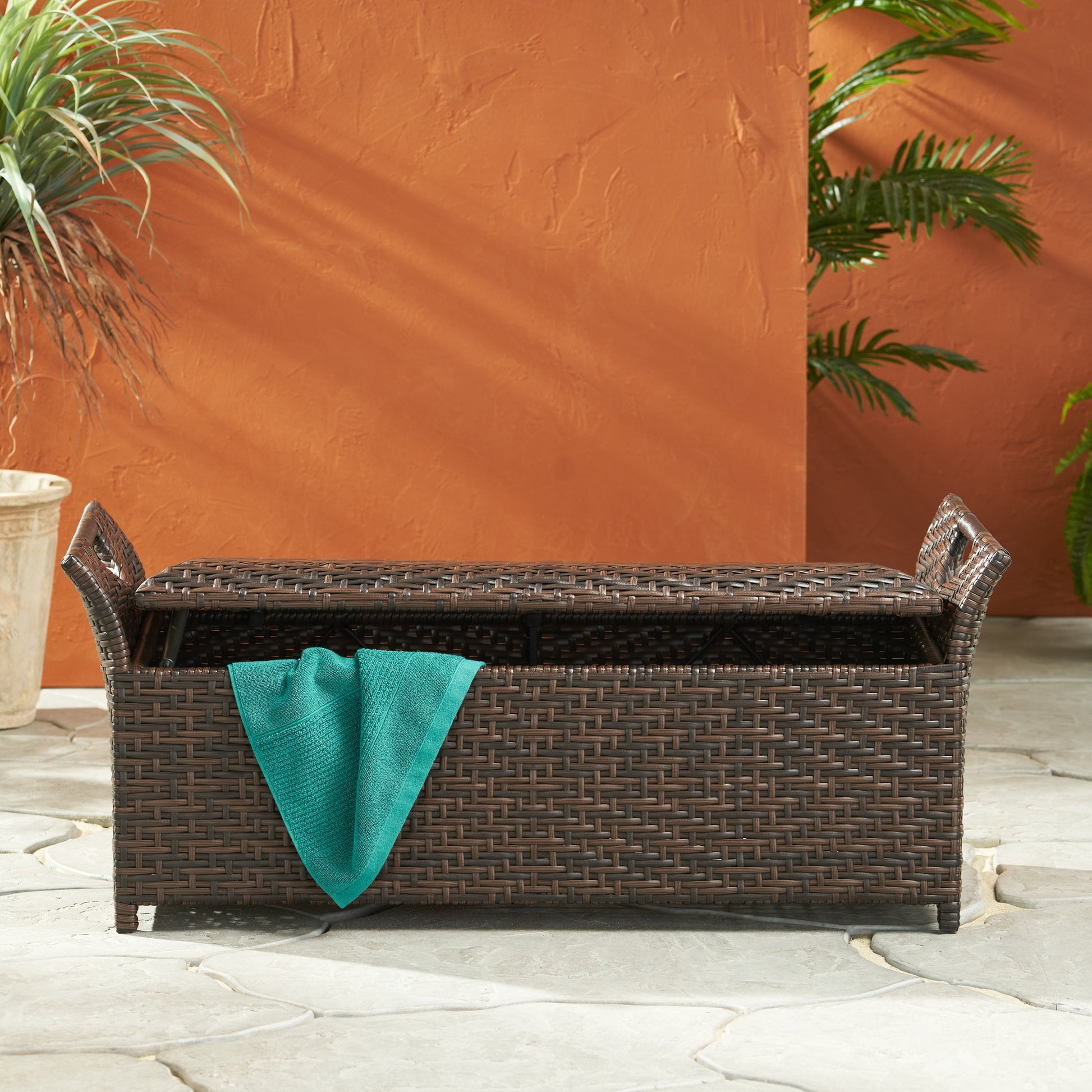 Brown wicker outdoor storage bench with a teal towel draped over it