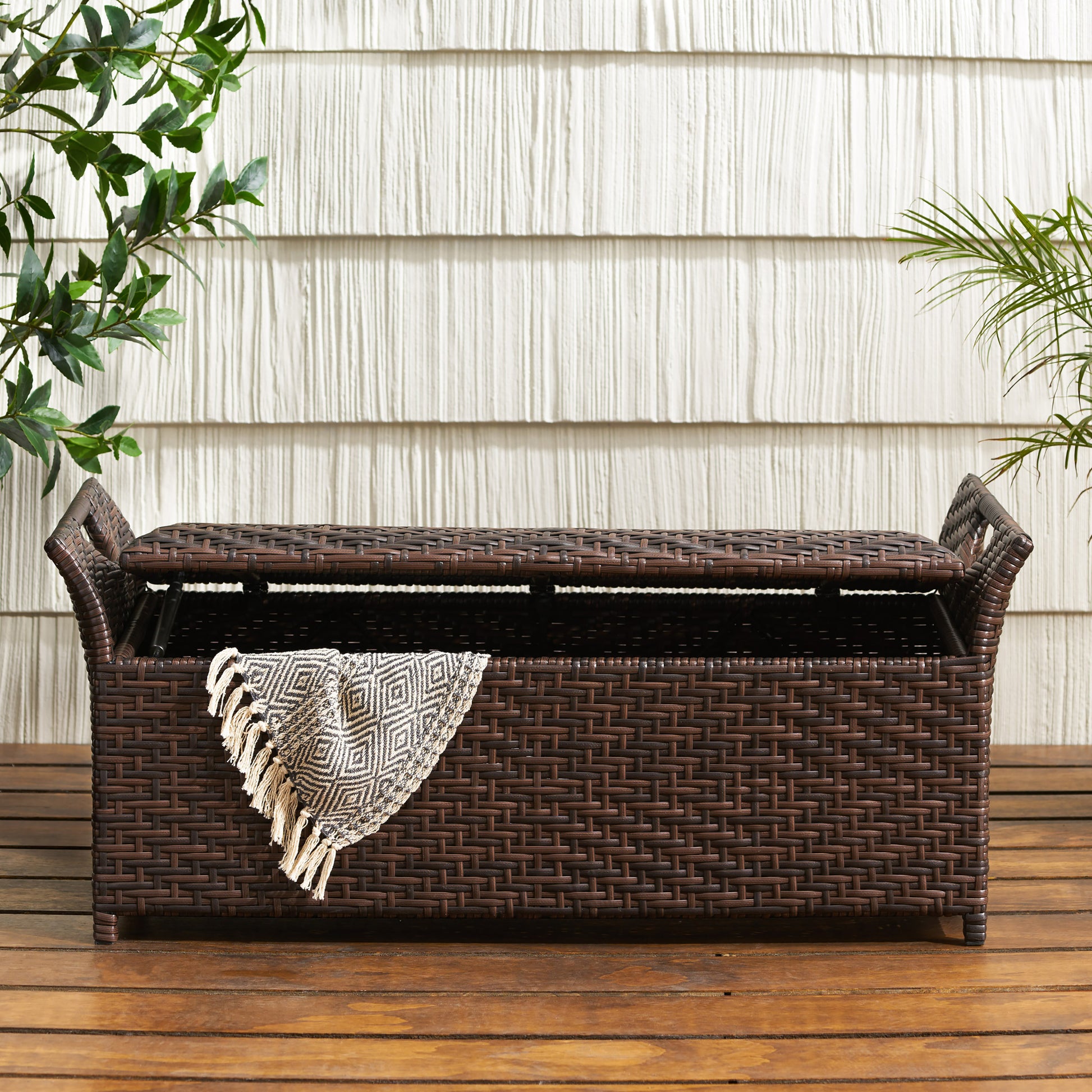 Dark brown rattan outdoor storage bench with hinged lid and textured woven design ideal for patio cushions