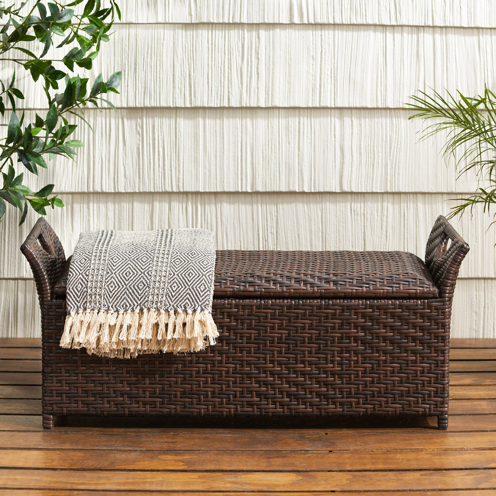 Dark brown wicker storage bench with a patterned throw blanket and tasseled fringe