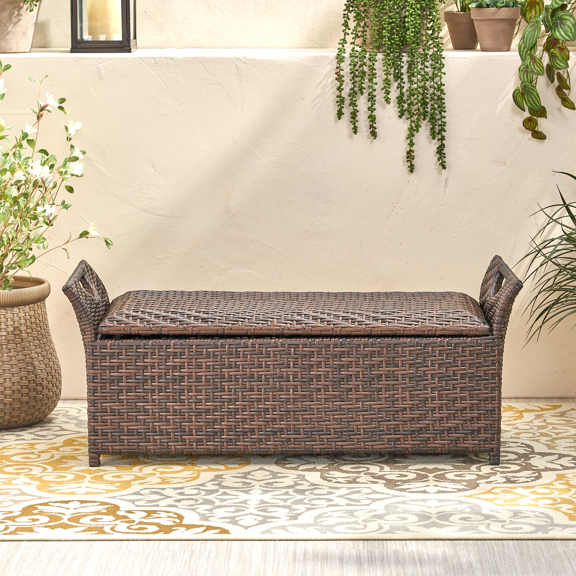 Brown wicker storage bench with decorative weaving and side handles for patio use