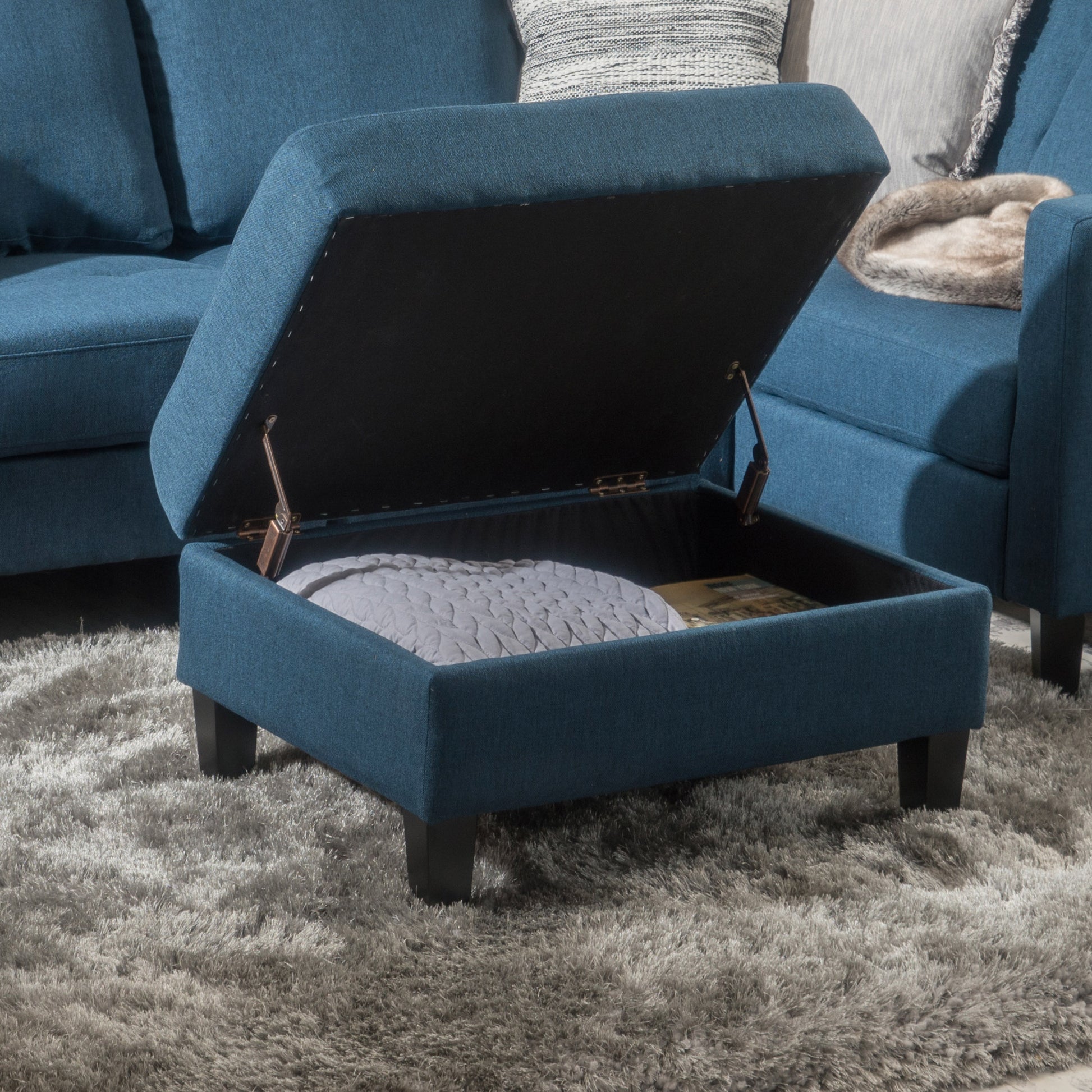 Blue fabric storage ottoman with lid open revealing blanket and books