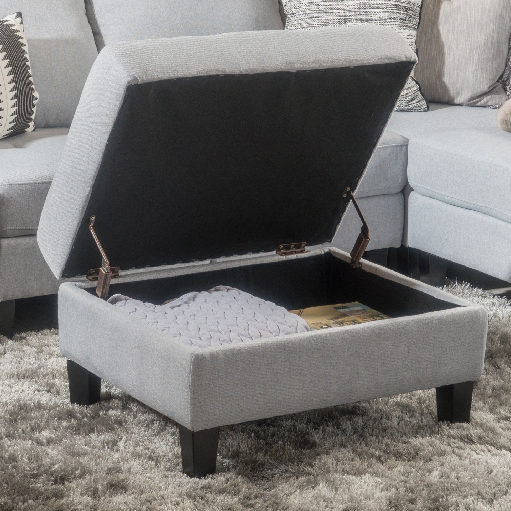 Gray fabric storage ottoman with open lid revealing blanket and books