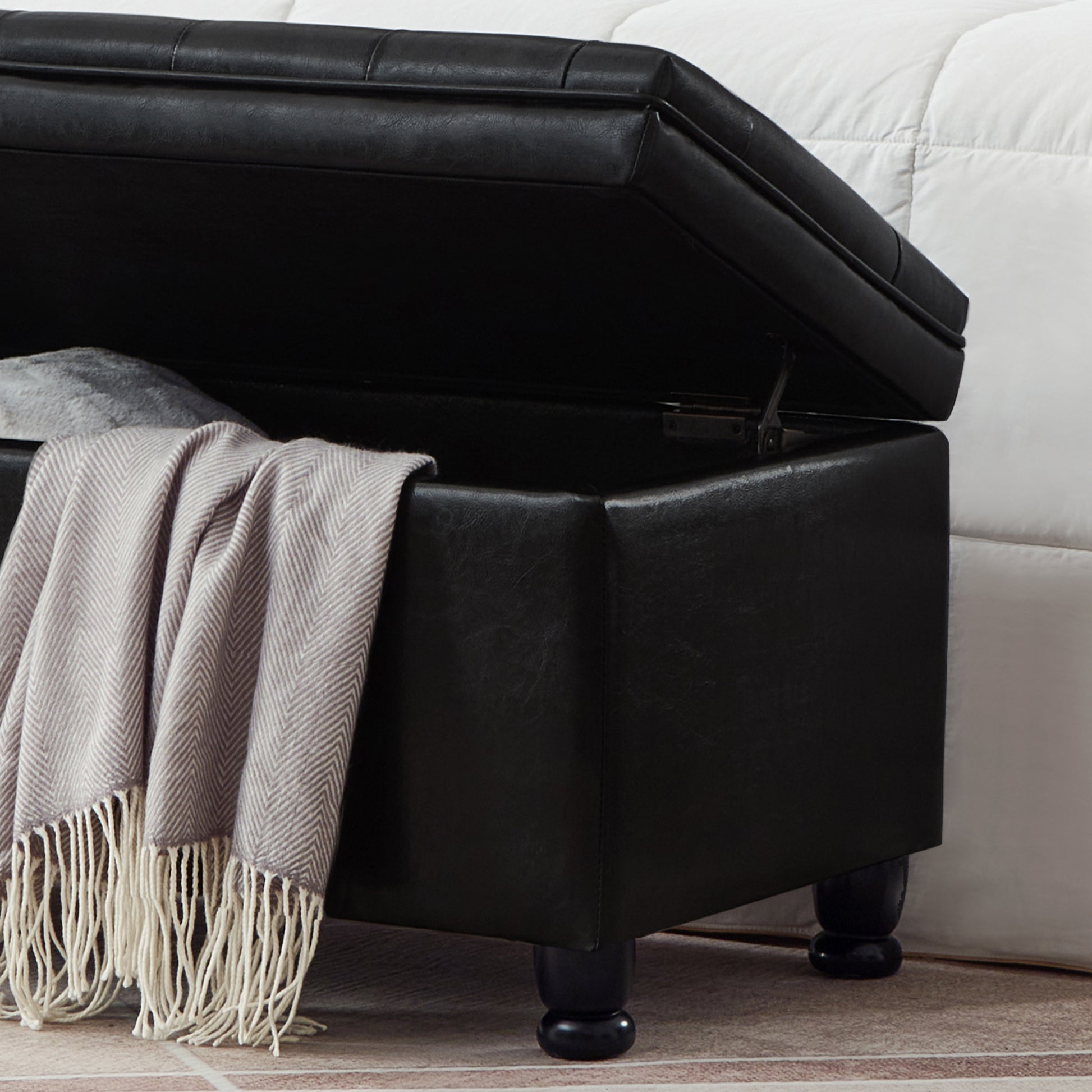 Black faux leather storage ottoman with tufted lid and plush blanket