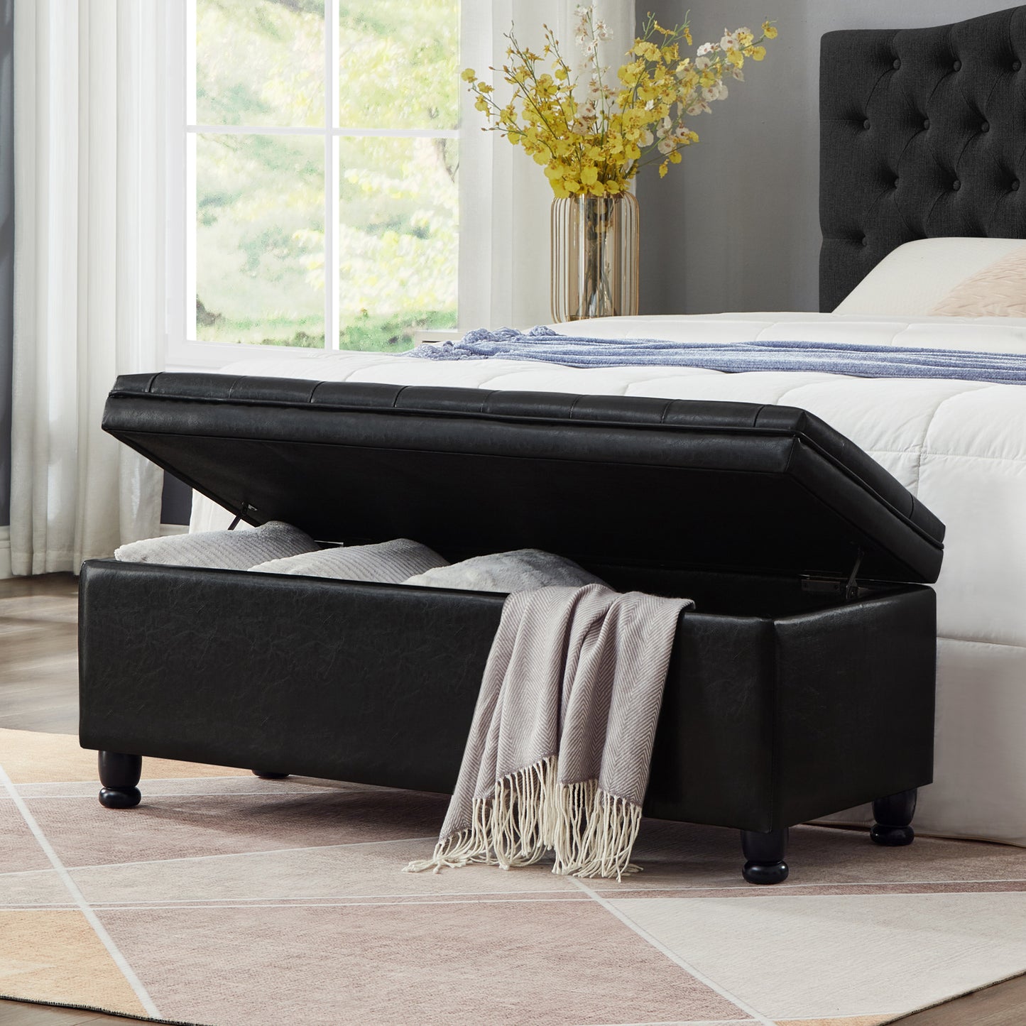Black faux leather storage ottoman with hinged lid open and revealing pillows