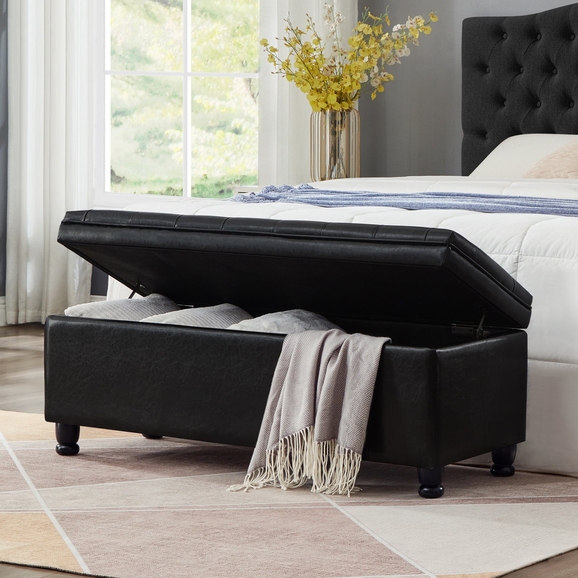 Black faux leather storage ottoman with hinged lid open and revealing pillows