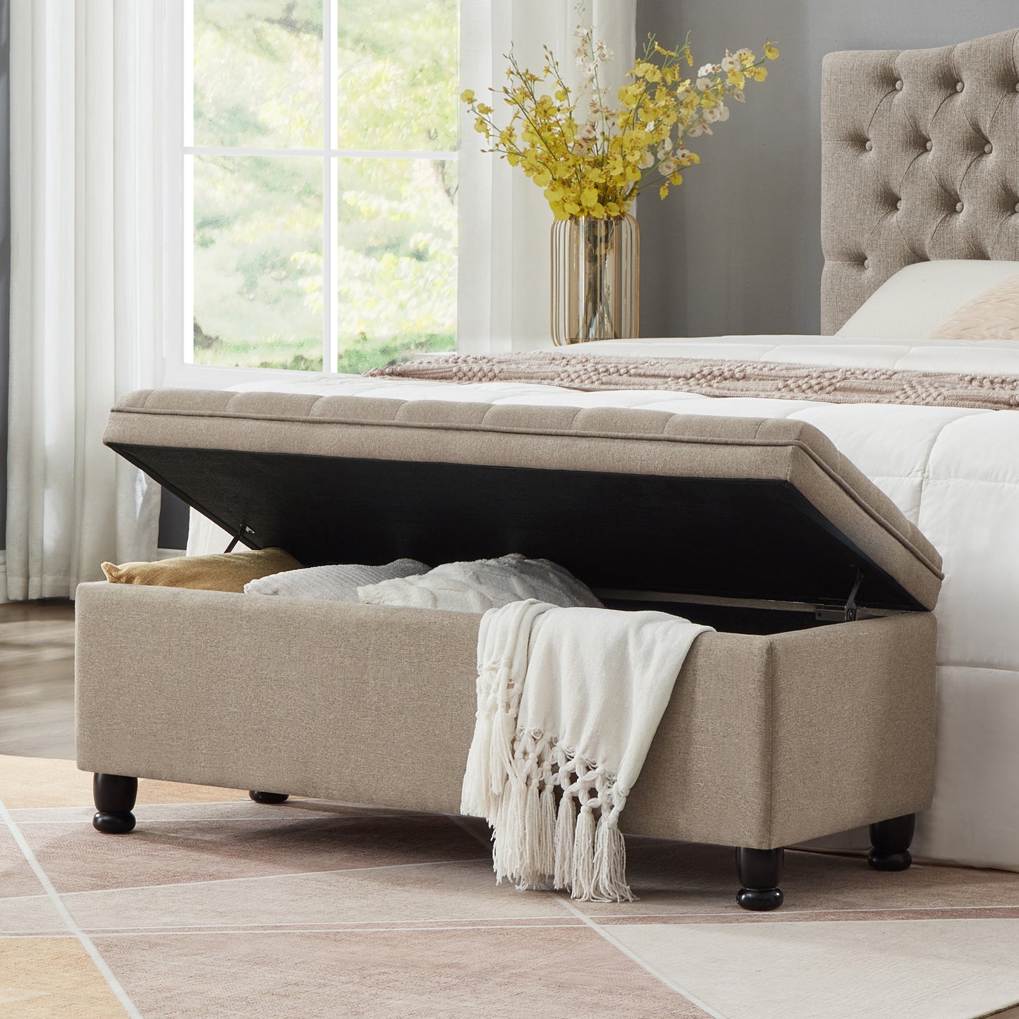 Beige upholstered storage ottoman with open lid revealing linens
