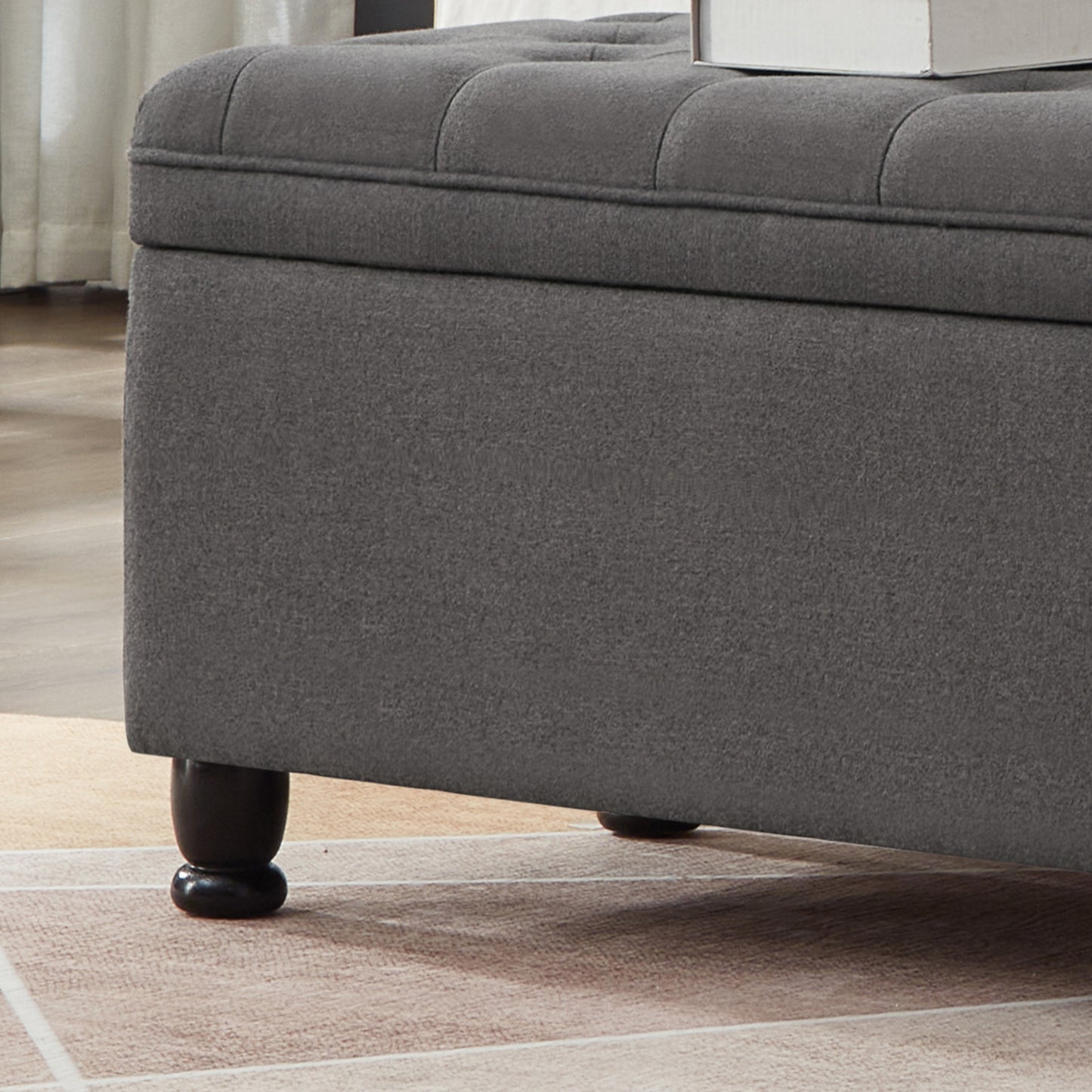 Dark grey fabric storage ottoman with tufted lid and dark wooden legs
