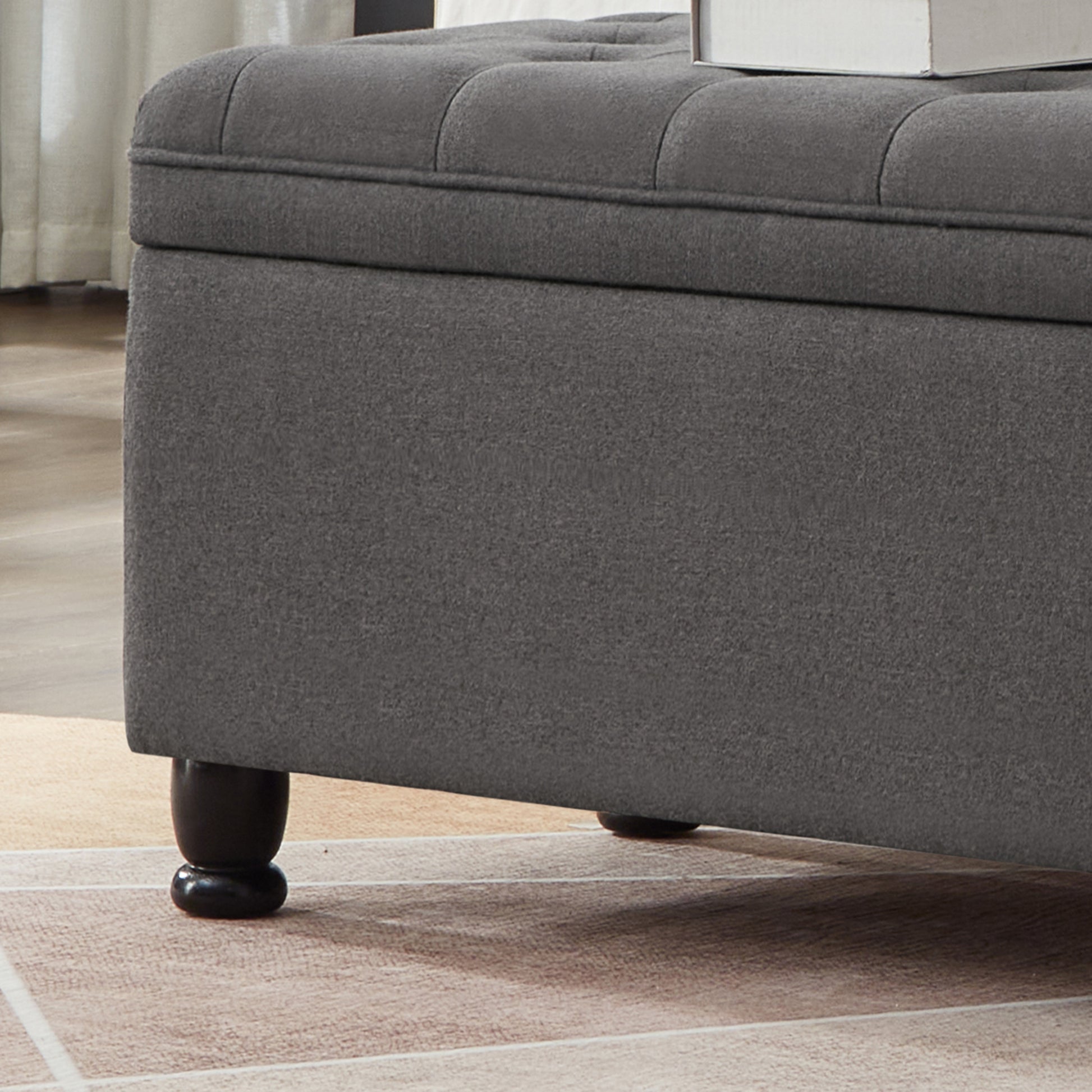 Dark grey fabric storage ottoman with tufted lid and dark wooden legs