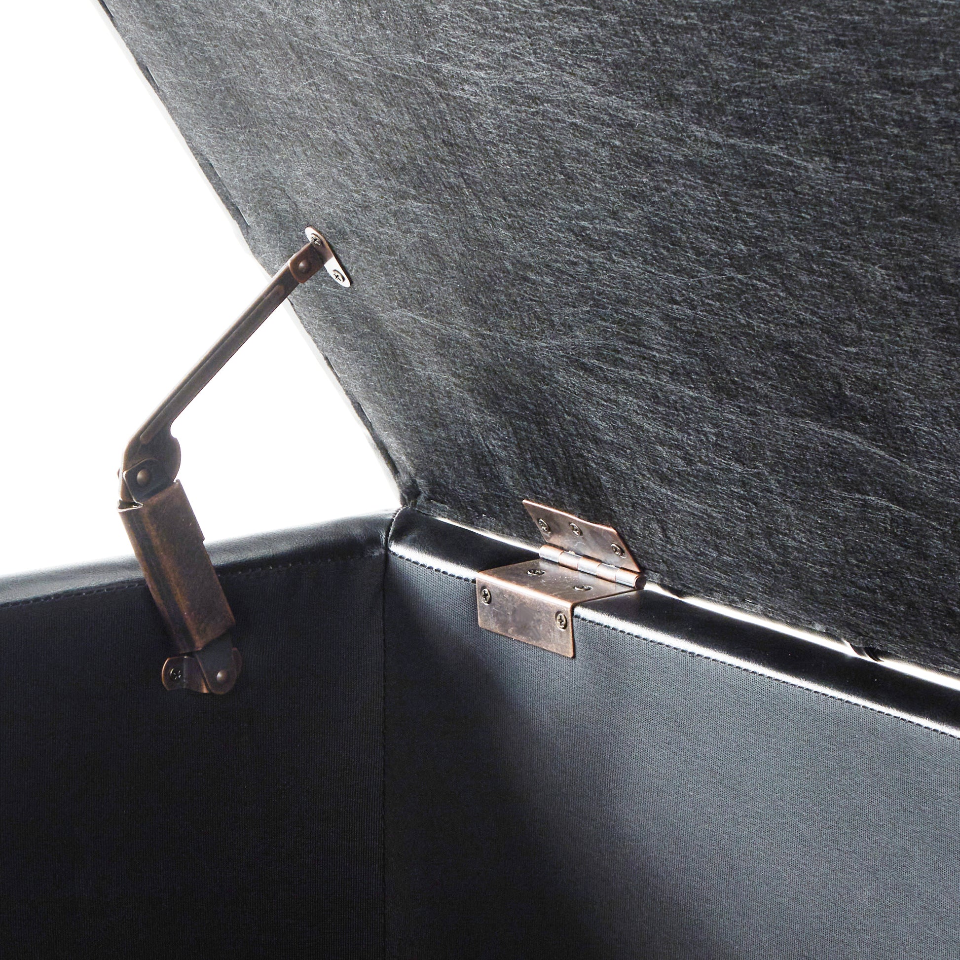 Closeup of a black storage ottoman with brass hinges