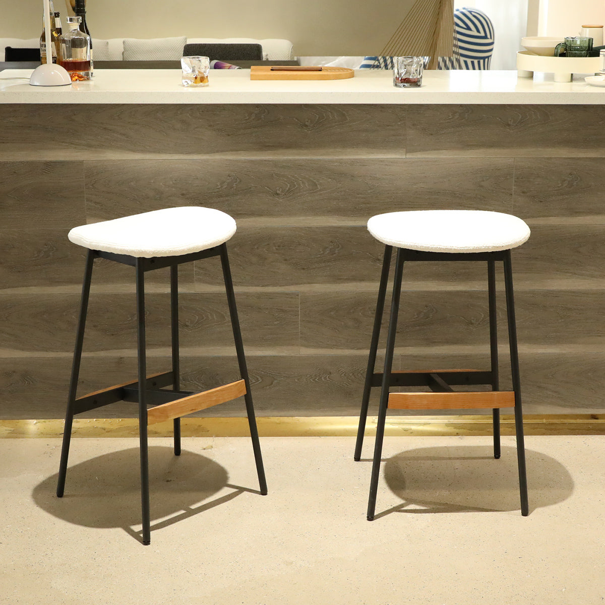 Two white upholstered bar stools with black metal legs and wood accents