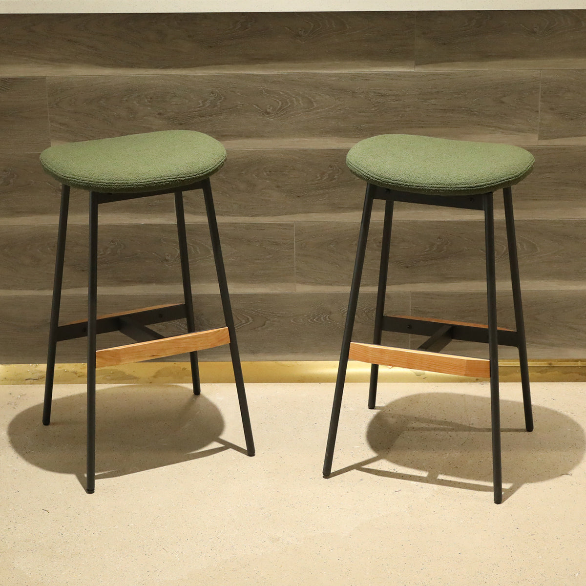 Two green fabric bar stools with black metal legs and wood accents