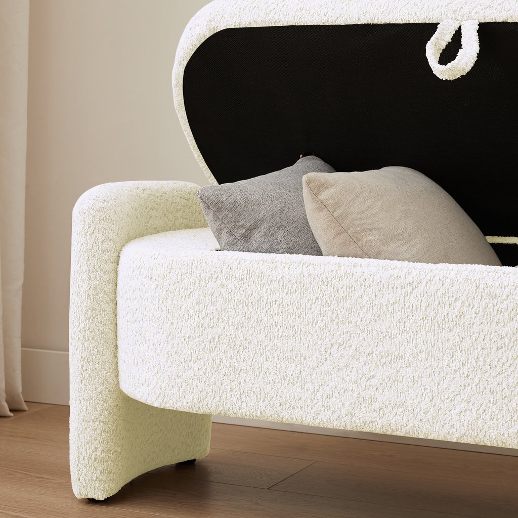 Cream boucle storage bench with open lid revealing black interior and two decorative pillows