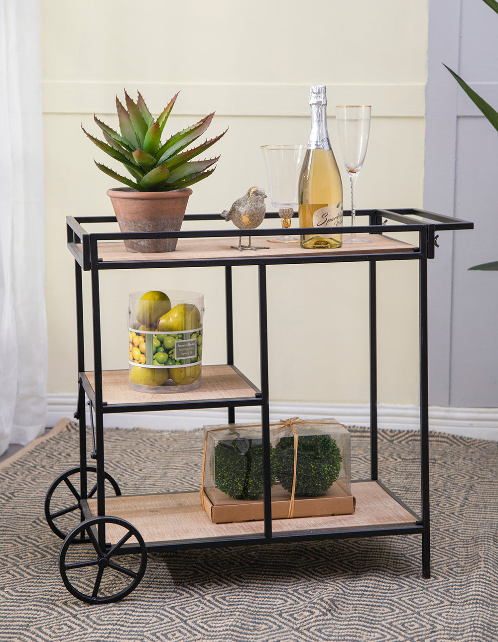 Black metal bar cart with wood shelves holding decorative items