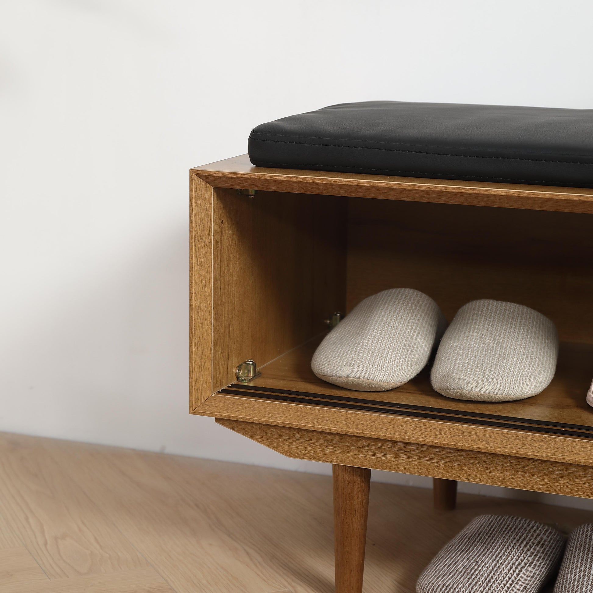 Wooden entryway bench with black padded seat and open shelf storing beige slippers