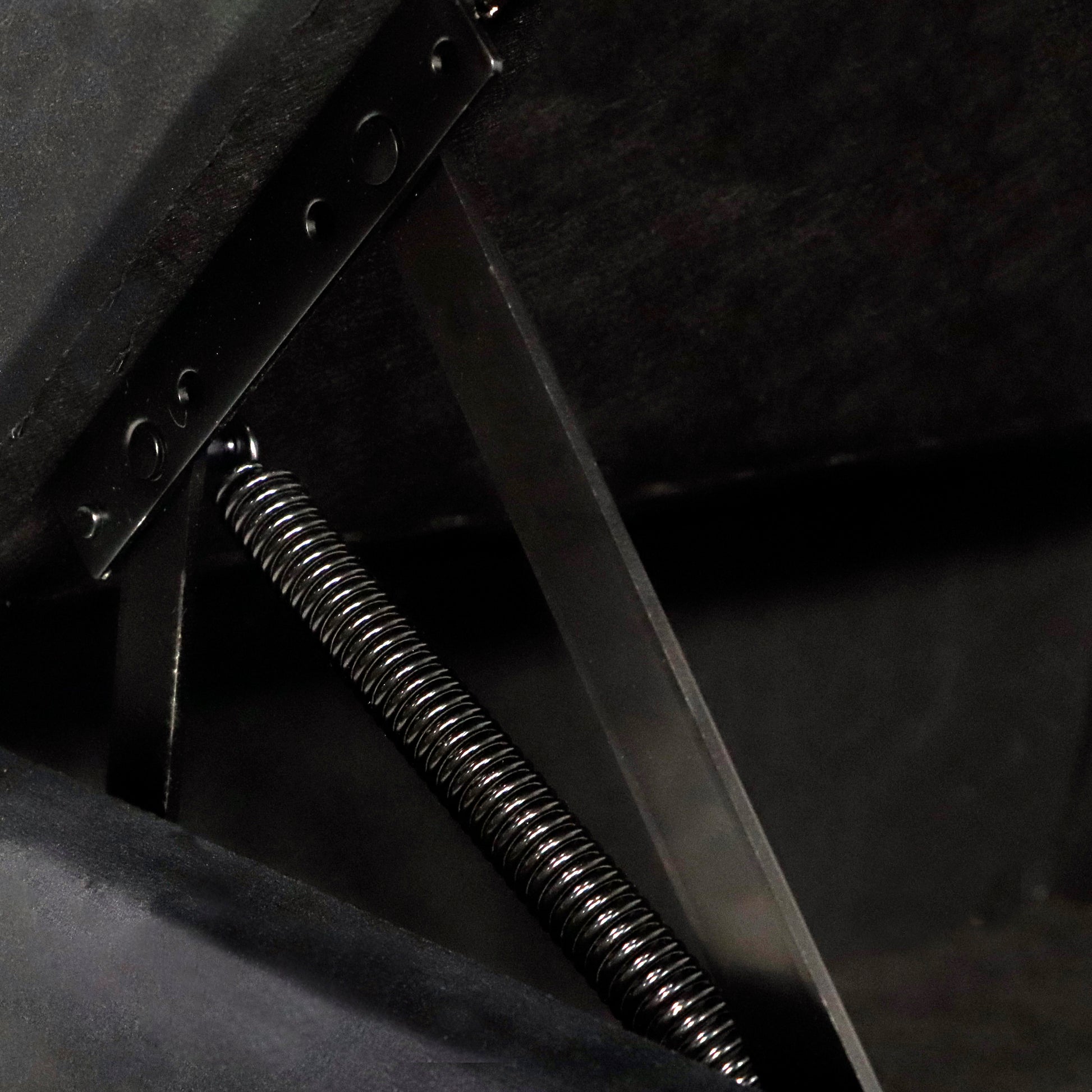 Closeup of a black metal spring mechanism on a dark upholstery fabric