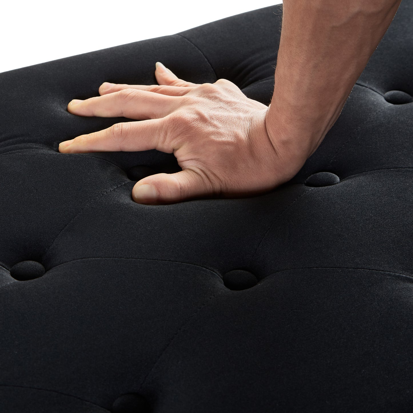 Black tufted ottoman demonstrating plush fabric cushioning with a hand pressing down