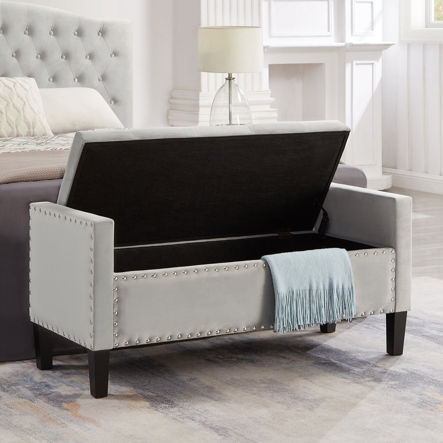 Light grey velvet storage bench with silver nailhead trim and dark wood legs