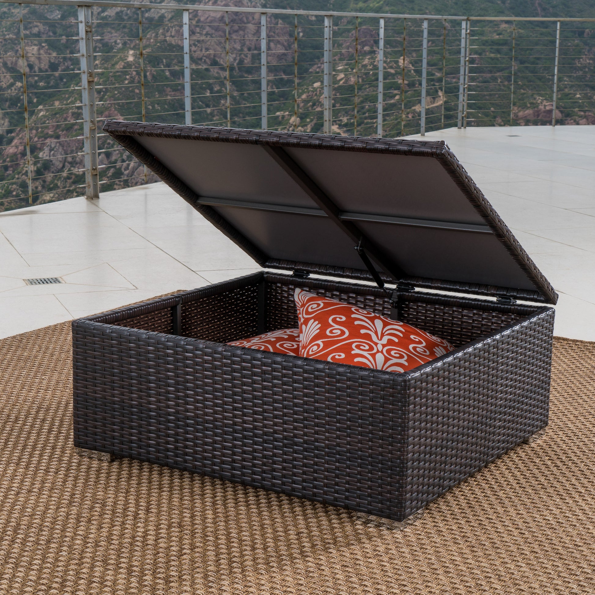 Dark brown wicker outdoor storage chest with orange patterned pillows inside