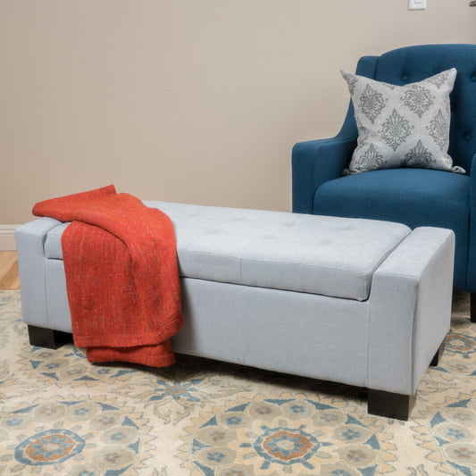 Light grey tufted storage ottoman with an orange throw blanket draped over it