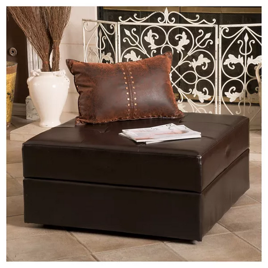 Dark brown leather storage ottoman with a decorative pillow and magazines on top