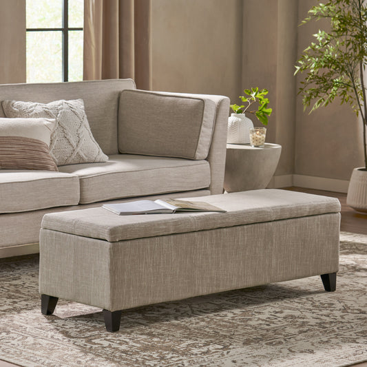 Beige linen storage ottoman with dark wood legs in a living room