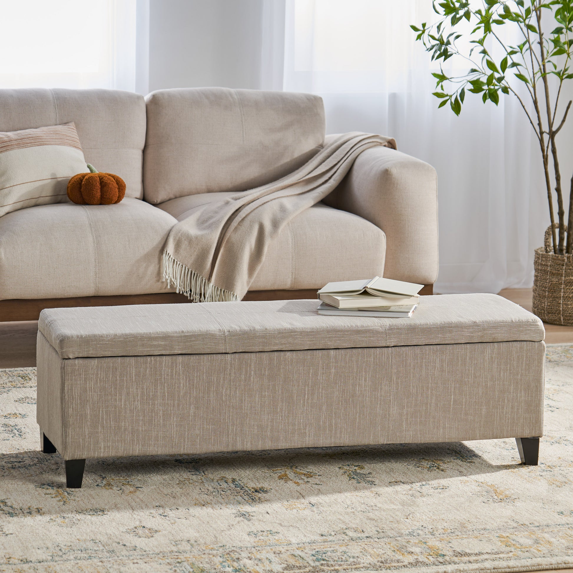 Beige fabric storage ottoman with dark wood legs in a living room