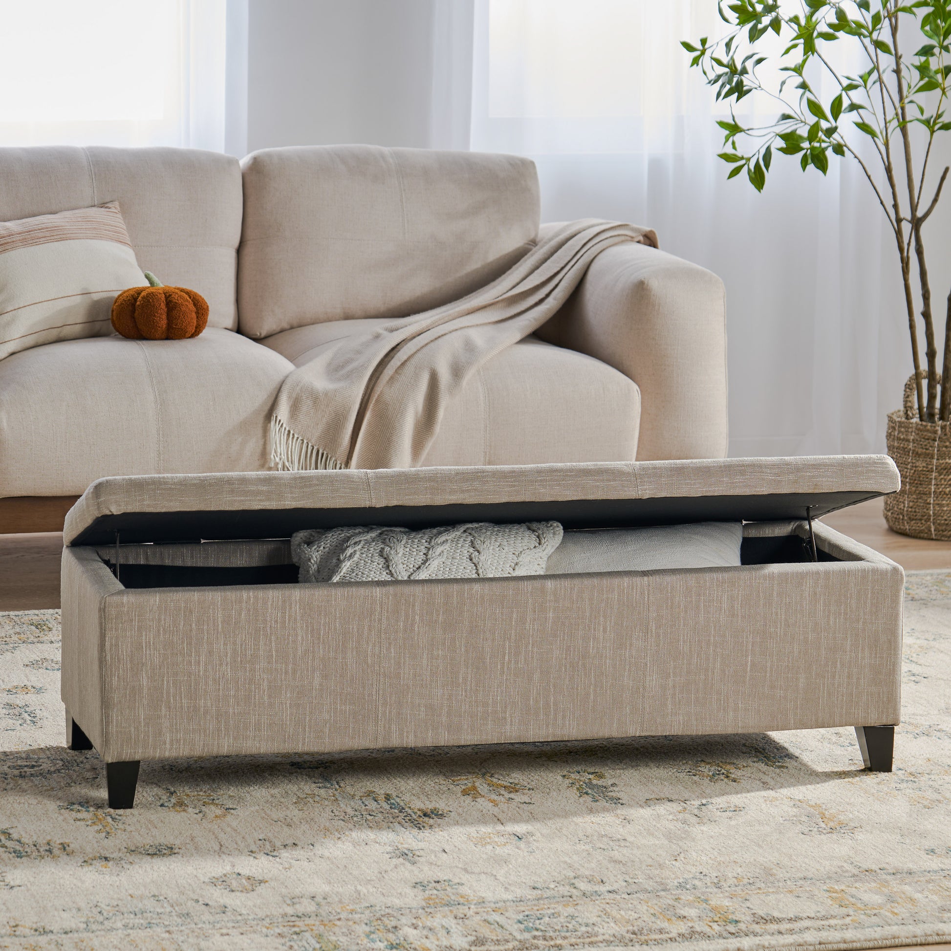 Beige linen storage ottoman with lifted lid revealing blankets