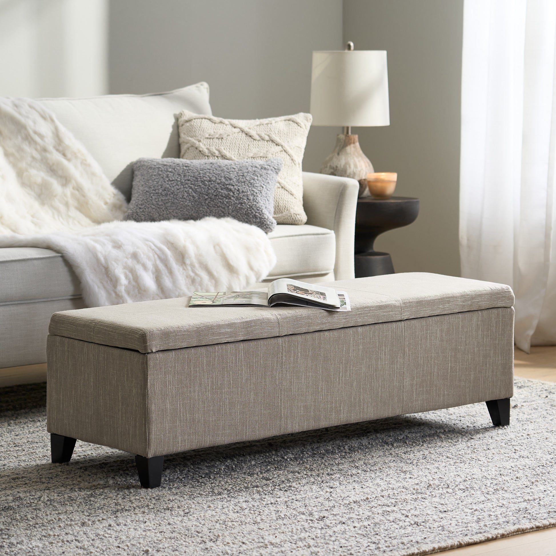 Beige fabric storage ottoman with dark wooden legs and open lid displaying magazines