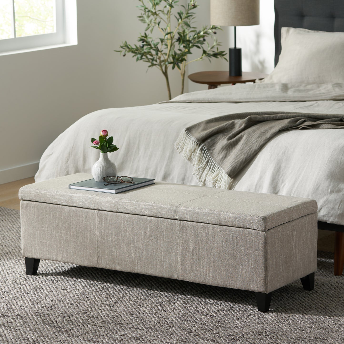 Linen storage bench in natural beige with dark wood legs at foot of bed