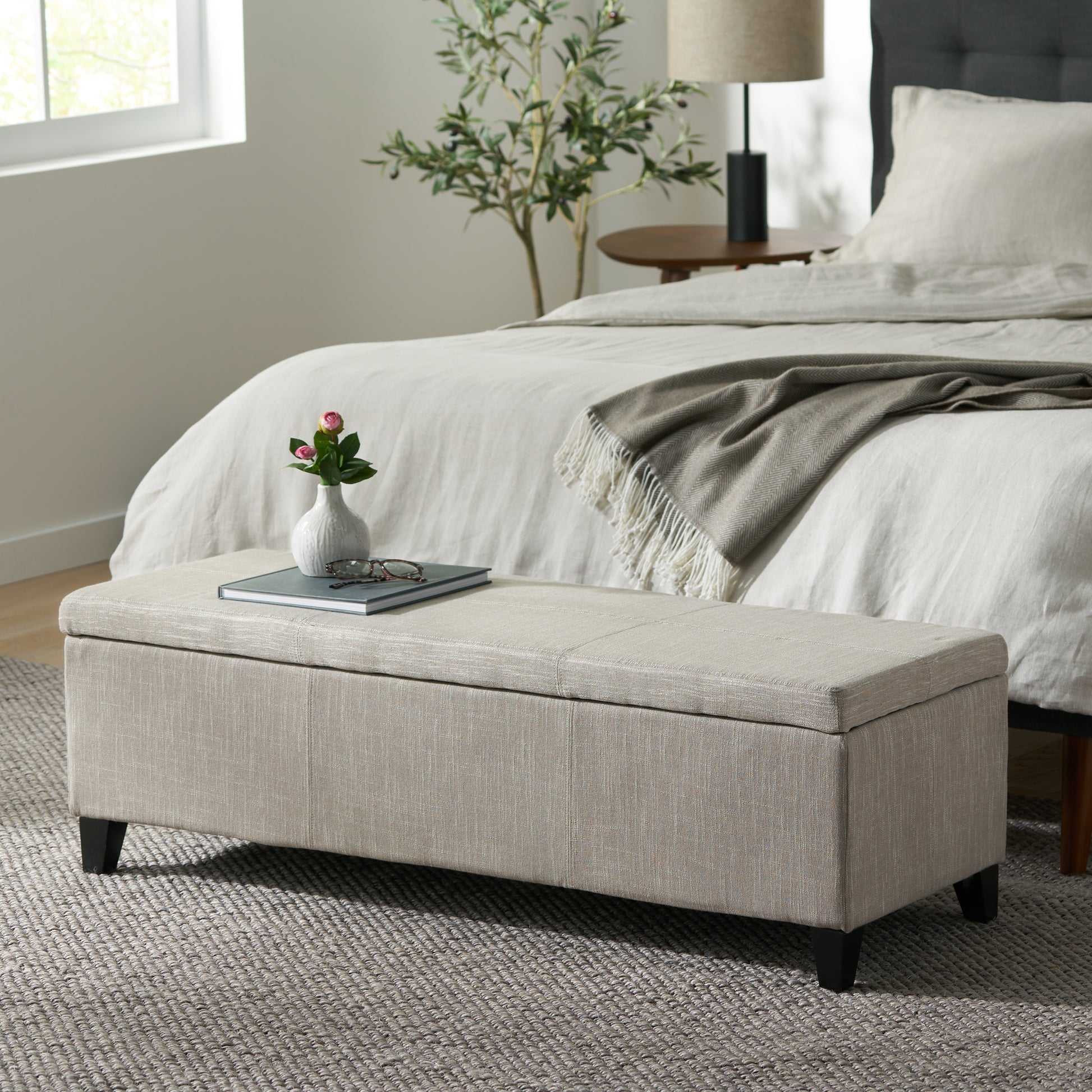 Linen storage bench in natural beige with dark wood legs at foot of bed