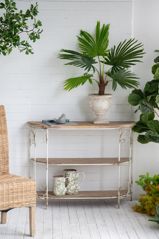 Antique white console table with three wooden shelves and distressed metal scrollwork