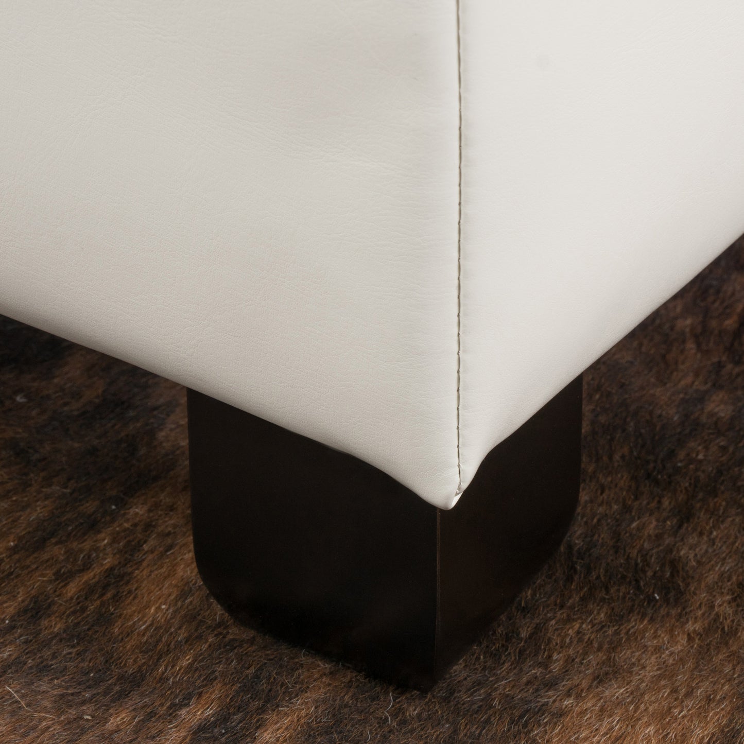 Closeup of white leather ottoman corner detail on dark wood base and textured rug