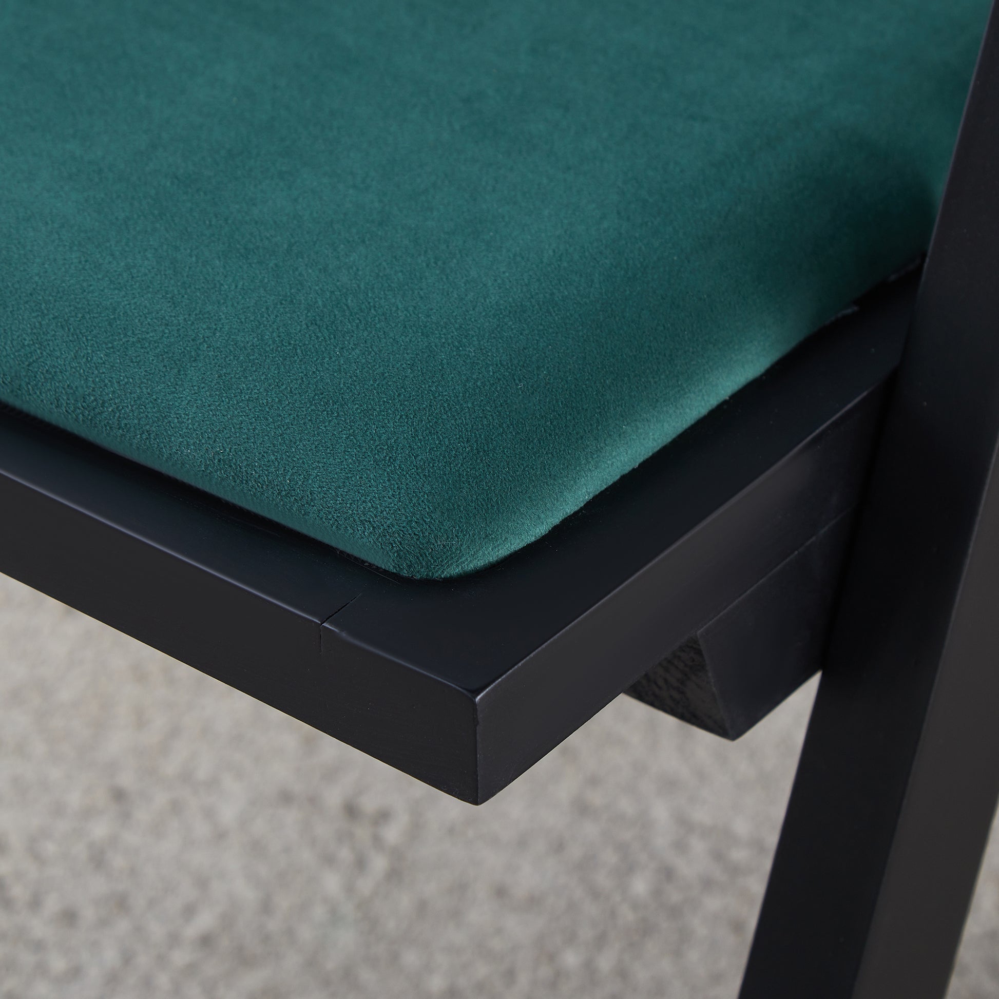 Closeup of a dark green velvet chair seat with a black wooden frame