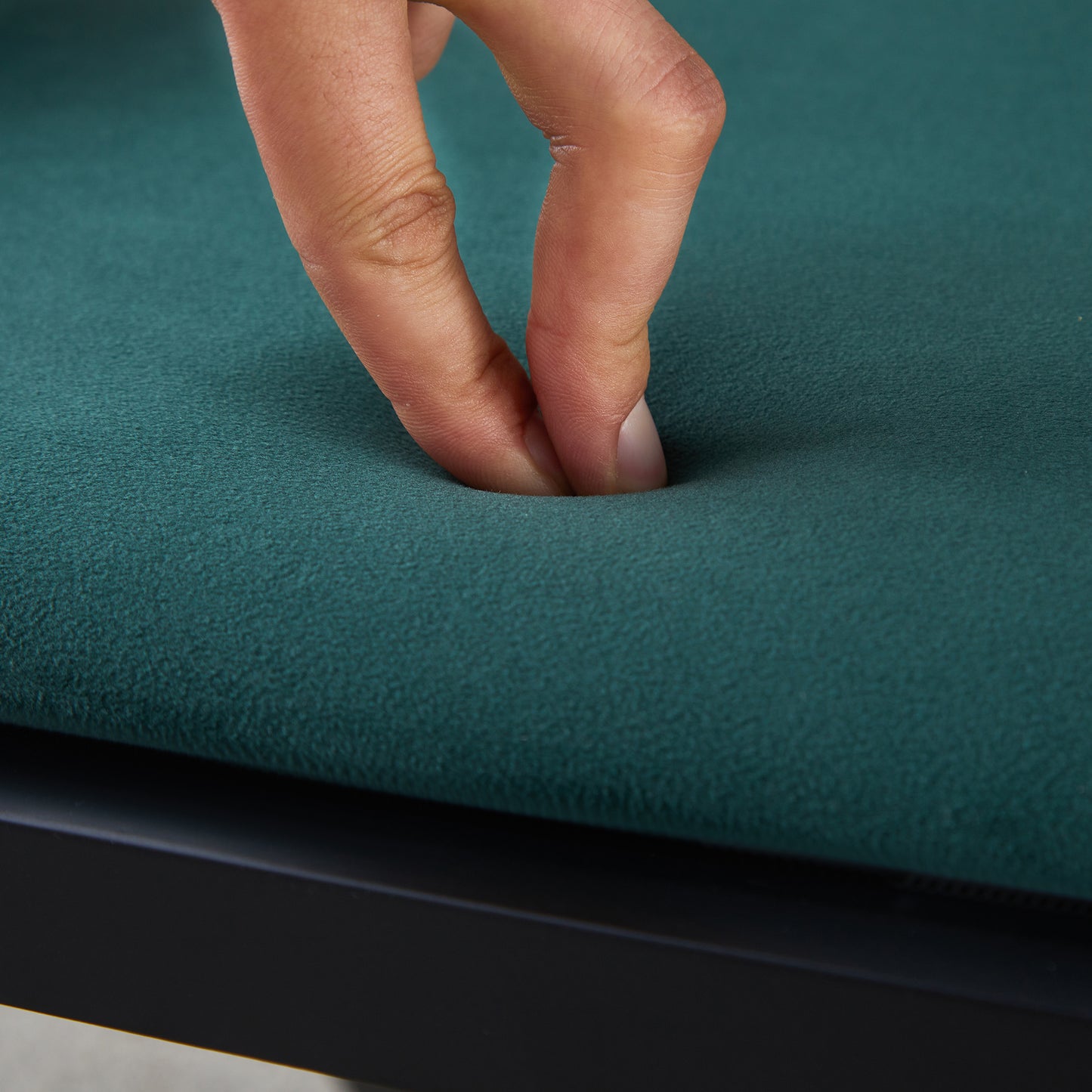 Closeup of teal velvet fabric showing plush texture with fingers pressing into seat cushion