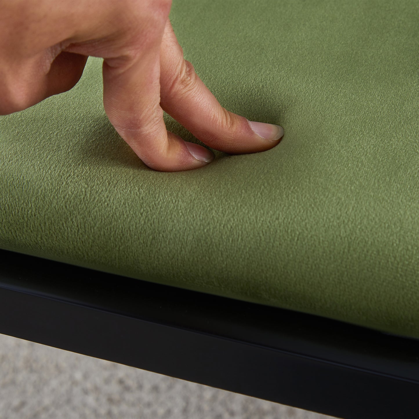 Fingers pressing into a plush sage green velvet fabric on a chair cushion