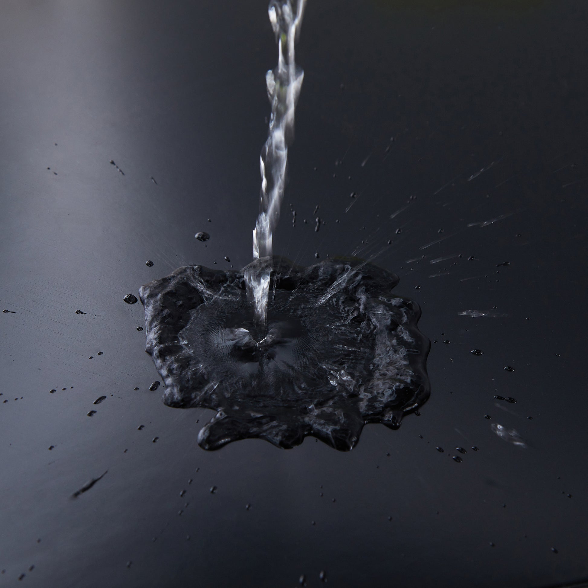 Splash of clear water forming a dark pool on a textured black surface