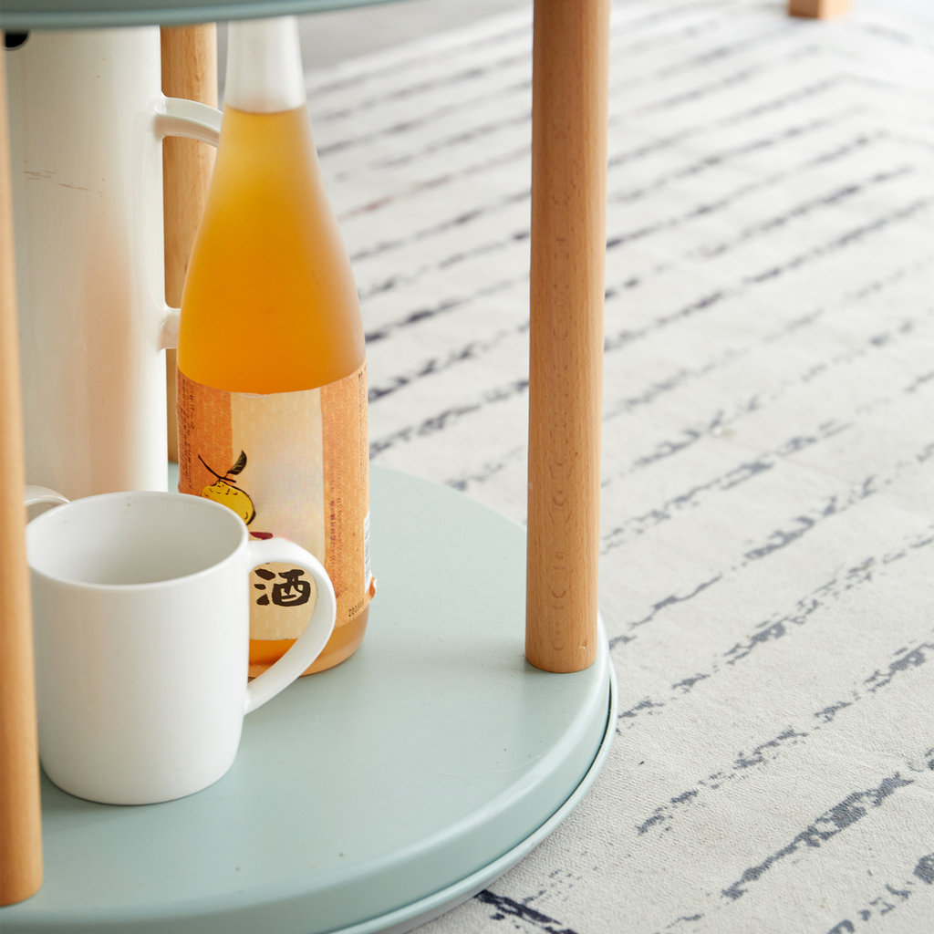 White ceramic mug with Japanese characters next to a tall bottle of amber liquid on a pale blue round table