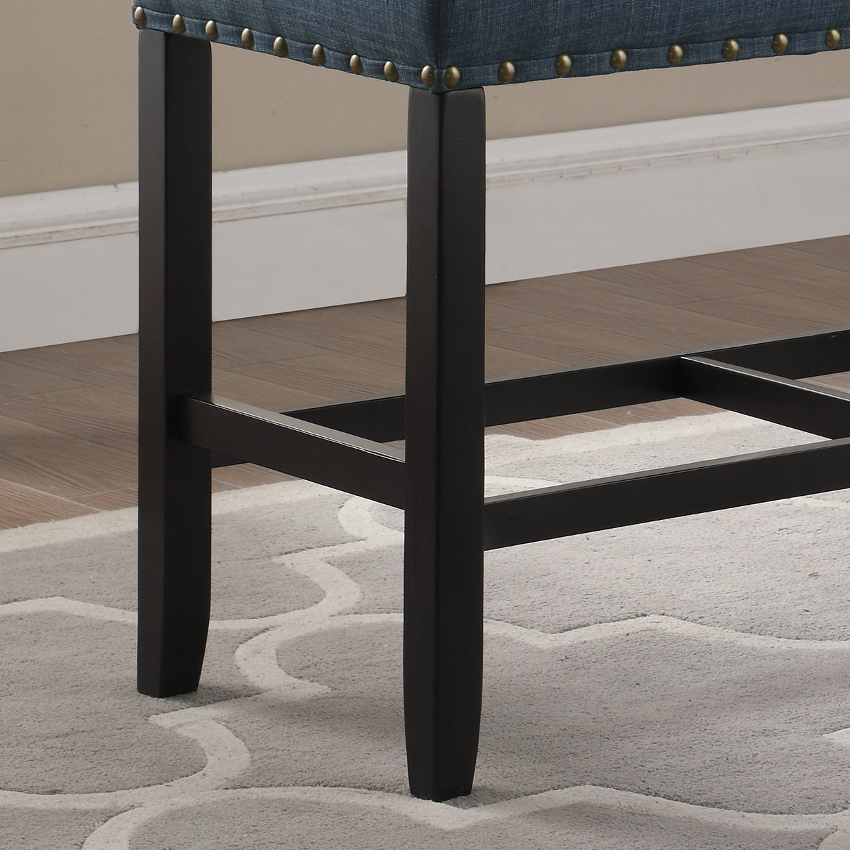 Dark wood bar stool legs with intricate nailhead trim on the seat edge