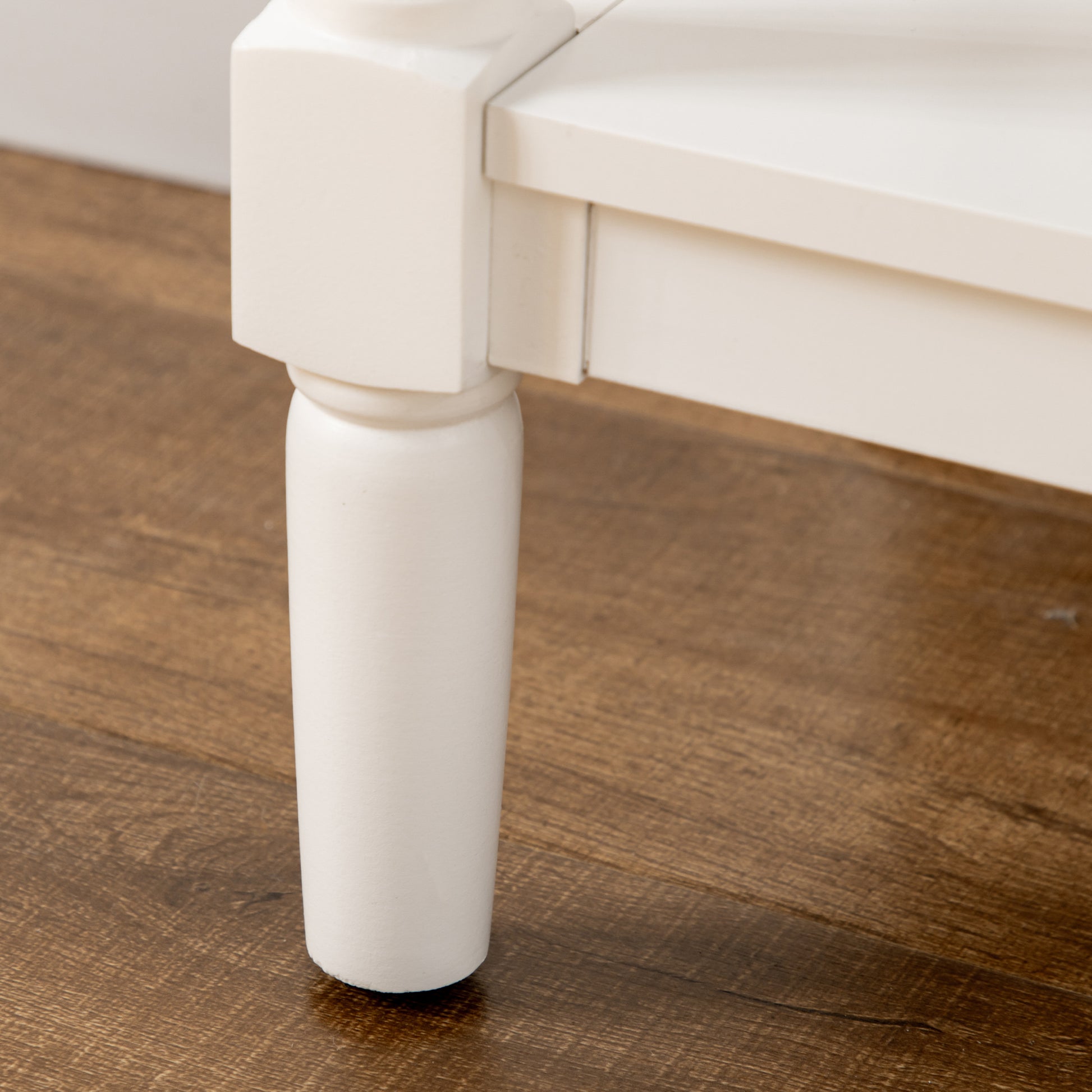 White carved wooden table leg detail on dark wood floor