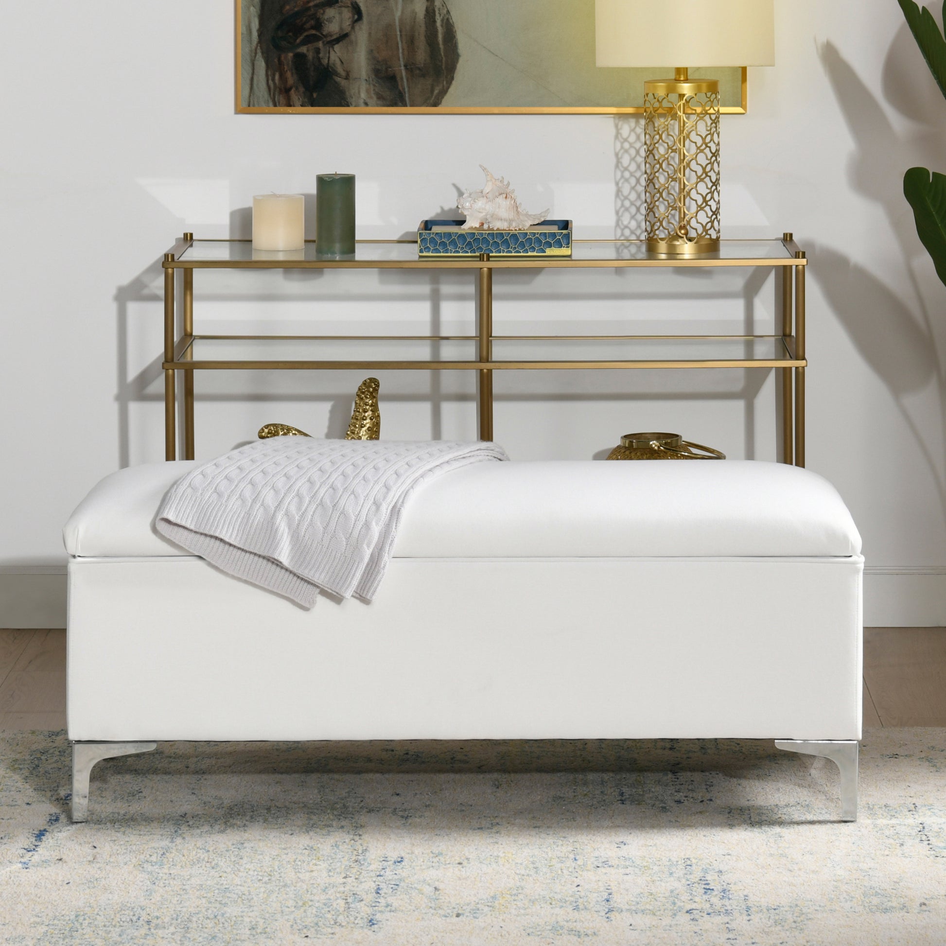 Modern white faux leather storage ottoman with silver legs and a folded knit throw