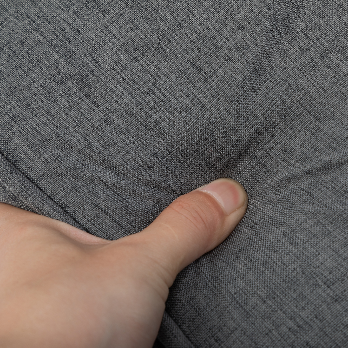 Closeup of grey linen fabric texture with a thumb pressing into it