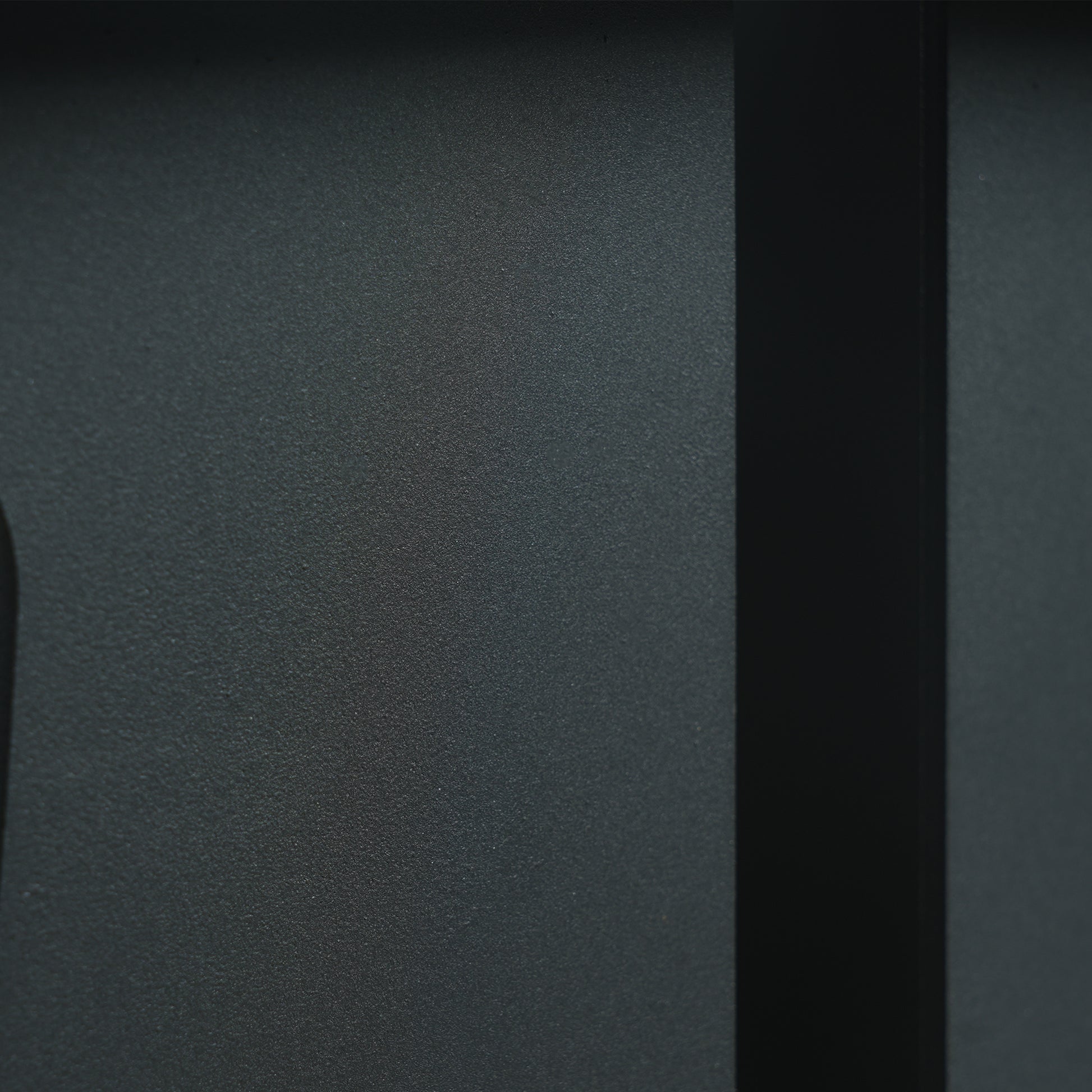 Closeup of a textured dark grey speaker grille with subtle light reflections
