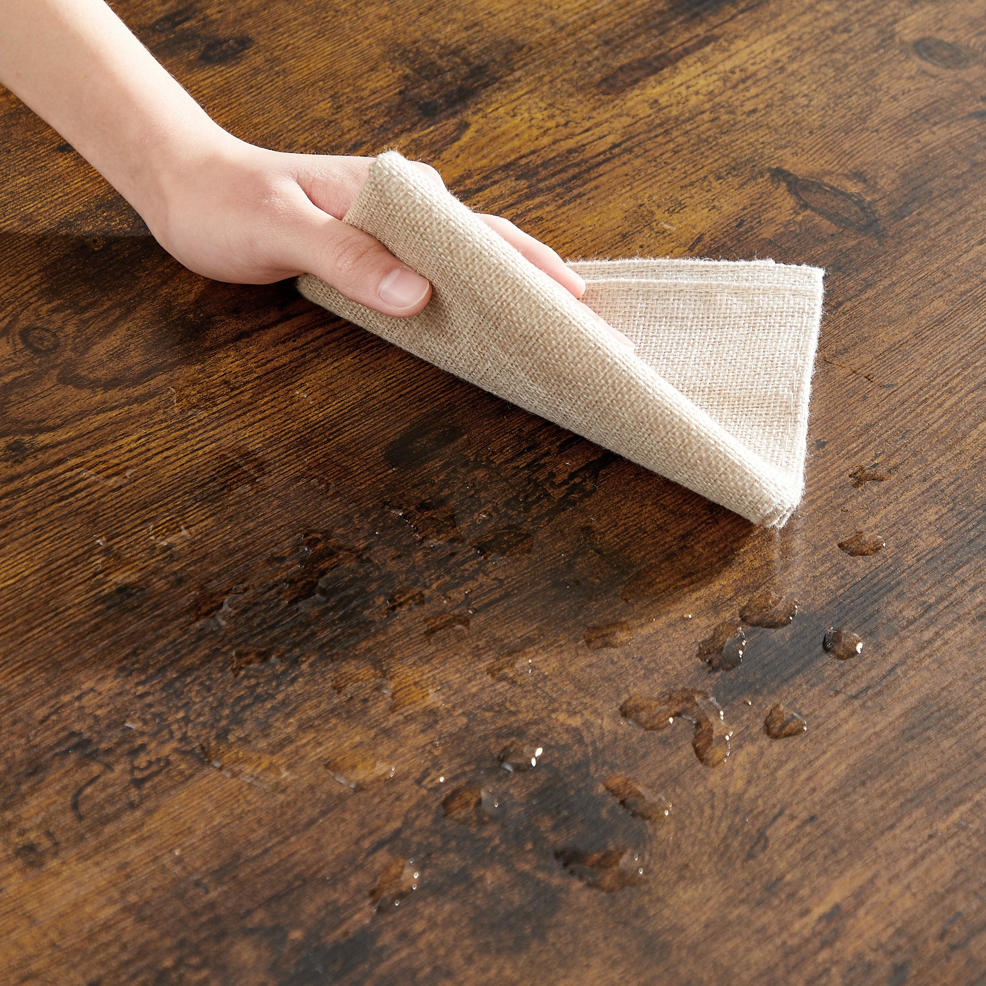 Beige linen cloth wiping water spills on a dark wood textured table